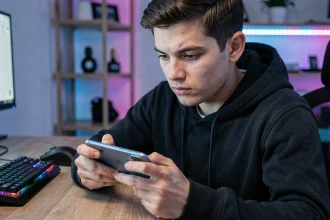 Jeune homme concentré jouant à un jeu mobile sur un smartphone grand écran dans un bureau gaming à domicile