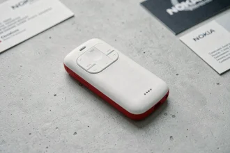 Nokia 5310 blanc et rouge posé sur une surface en béton, vue de dessus en angle 3/4 montrant les touches multimédias